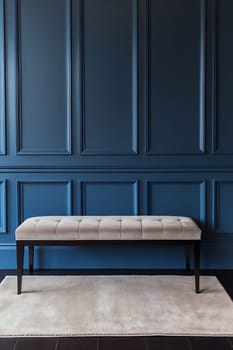A modern, tufted light grey bench is positioned in front of a deep blue paneled wall, adding elegance to the minimalist interior.