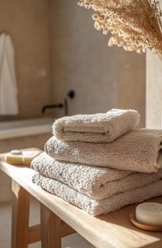 Plush beige towels are stacked on a wooden table in a serene bathroom atmosphere, showcasing a tranquil and organized setting.