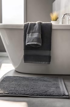 Two luxurious gray towels hang over a sleek bathtub, adding elegance to a contemporary bathroom setting with natural light.