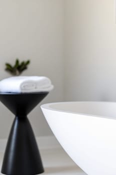 A sleek, modern bathroom features a contemporary white vessel sink and a stylish black stool holding rolled towels, creating a serene atmosphere.