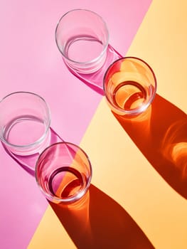 Four glass cups rest on a bright pink and orange surface, showcasing their unique colors and casting striking shadows.