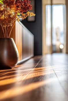Soft sunlight streams through a doorway, highlighting elegant decor and a vase of dried flowers on the polished wooden floor.