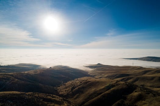 The sky is blue and the sun is shining brightly. The clouds are white and fluffy, and the sun is casting a warm glow on the landscape