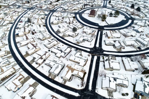 A snow covered neighborhood with houses and a round street. The houses are all small and the street is surrounded by snow