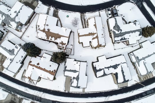 A snow covered neighborhood with houses and a street. The houses are all lined up in a row and the street is empty
