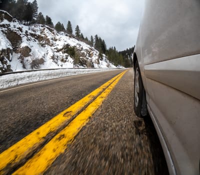 A car is driving down a snowy road with yellow lines. The car is moving fast and the snow is covering the road