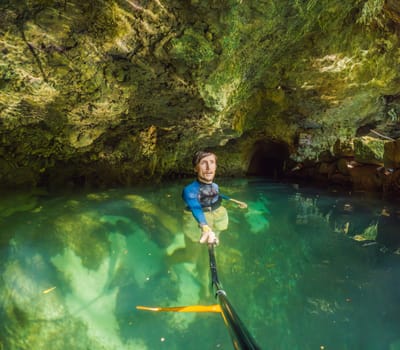 Man tourist in the water of a Mexican cenote surrounded by natural beauty. Adventure travel, eco-tourism, and exploration concept in a tropical paradise.