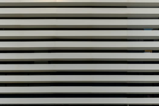 Vertical lines converge as sleek white slats create a rhythmic pattern on a modern urban structure during daylight.