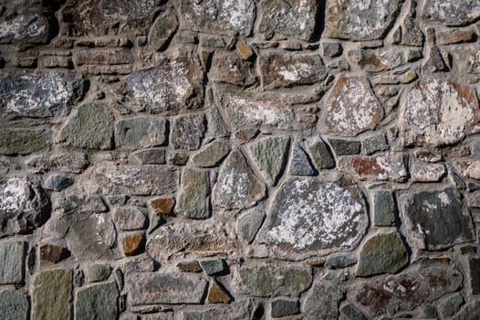 Discover the intricate textures of a weathered stone wall adorned with moss and lichen in soft sunlight.