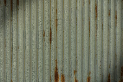 Textured corrugated metal wall reveals time's influence through rust patterns and faded colors in an industrial setting.