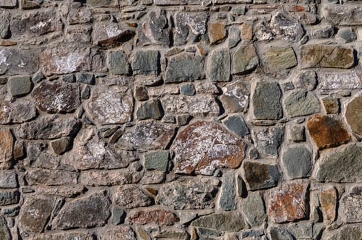 Rough stones form a captivating wall, displaying rich textures and hues under warm sunlight at a historic location.