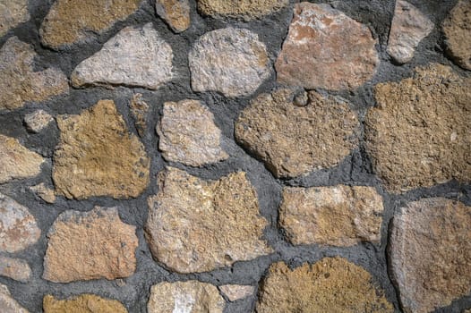 Natural stones fill the rustic wall, enhancing the charm and texture in the sunlit outdoor space.