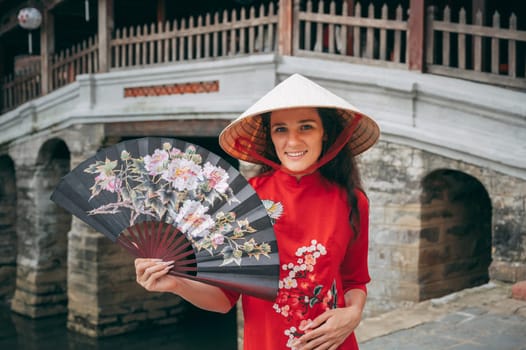 happy female traveler tourist in a Vietnamese hat at the ancient Japanese covered bridge in Hoi An in Vietnam in Asia