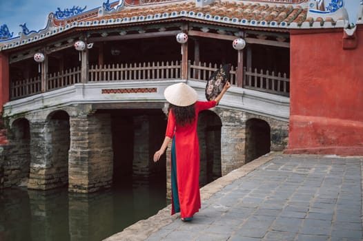 back of woman traveler tourist in a Vietnamese hat at the ancient Japanese covered bridge in old town in Hoi An in Vietnam in Asia
