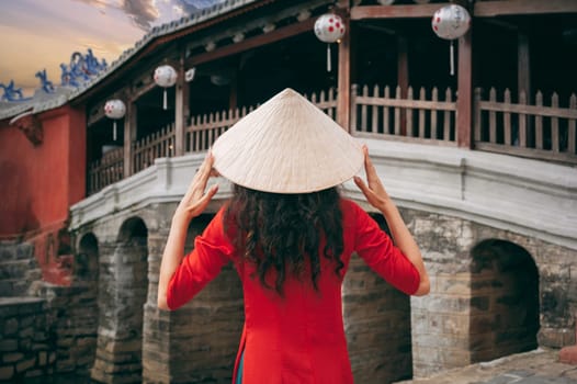 back of girl traveler tourist in Vietnamese hat at ancient Japanese covered bridge in old town in Hoi An in Vietnam in Asia
