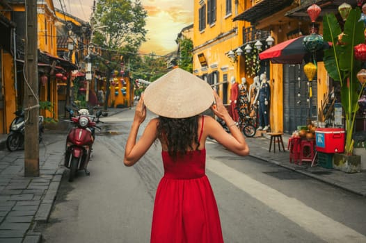 back of beautiful woman tourist in traditional Vietnamese hat and red dress on street in old town in Hoi An city in Vietnam in Asia
