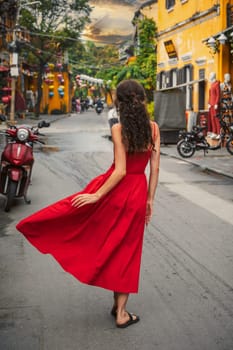 back of a young beautiful female tourist traveler in a red dress on the street in the old town in Hoi An in Vietnam in Asia