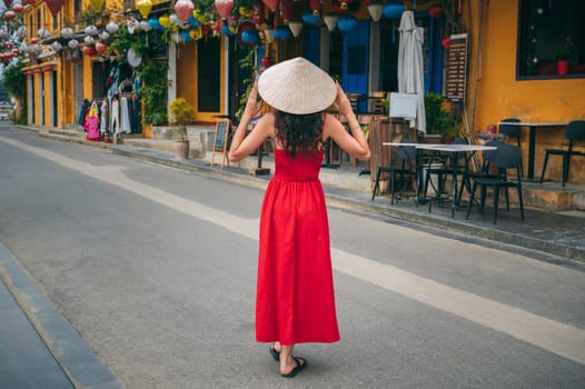 beautiful asian female tourist in Vietnamese hat and red dress on the street in the old town in Hoi An city in Vietnam in Asia