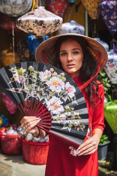 portrait of a beautiful tourist woman in Vietnamese cone hat Non La with a fan in Hoi An in Vietnam in Asia