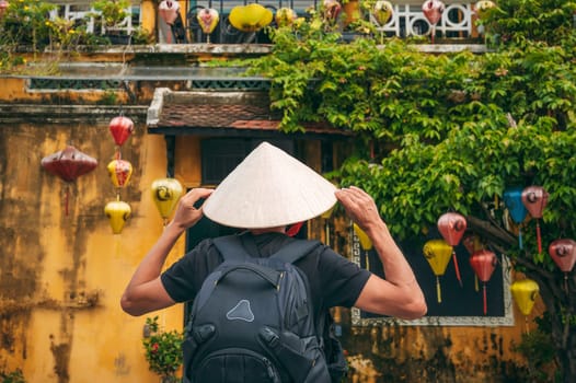 back of Asian male traveler tourist in traditional vietnamese hat on a street in old town in Hoi An city in Vietnam in Asia