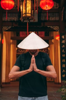 male tourist traveler in a Vietnamese hat prays at a temple on a Buddhist pagoda in Hoi An in Vietnam in Asia