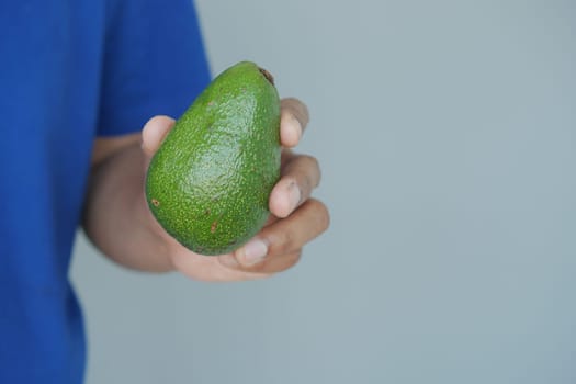 A person displays a fresh avocado in their hand, showcasing its color.