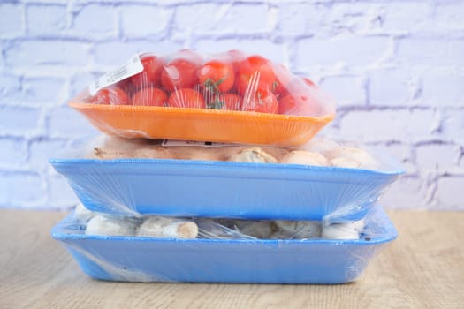 Colorful trays hold fresh tomatoes and mushrooms wrapped in plastic.