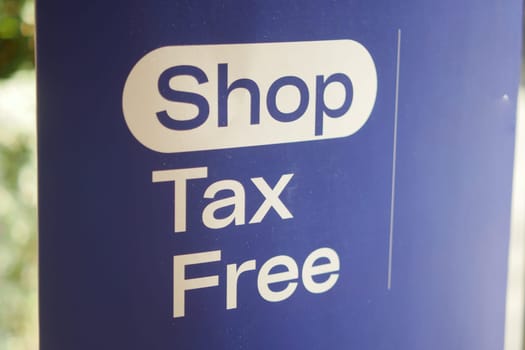 Sign promotes tax-free shopping in a bustling retail location outdoors.