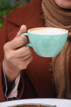A person enjoys a warm cup of coffee on a cool day outdoors.