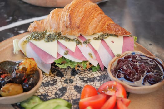 A croissant sandwich filled with ham and cheese, paired with dips.