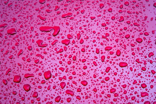 red background with texture of rain drops on purple metallic surface close up