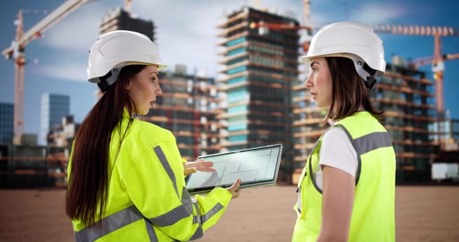 Young female engineer inspects construction site using tablet and clipboard.