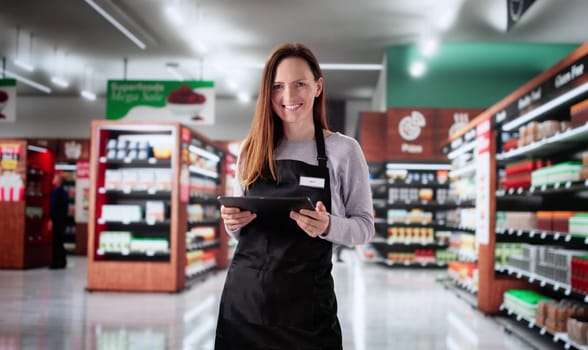 Smiling cashier at grocery store using tablet to assist customers.