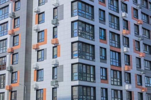 The concept of modern architecture, a residential complex, an apartment building for living. Close-up of the corner of the house in the camera multi-storey, apartment building in gray and white tones with orange inserts of modern architecture with large windows and framed balconies and baskets for air conditioning. High quality photo