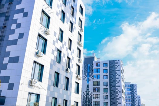 The concept of modern architecture, residential complex, apartment buildings for living. The camera moves smoothly along a multi-storey, multi-apartment residential complex of modern architecture in gray and white tones with large windows against the background of blue sky and clouds. High quality photo