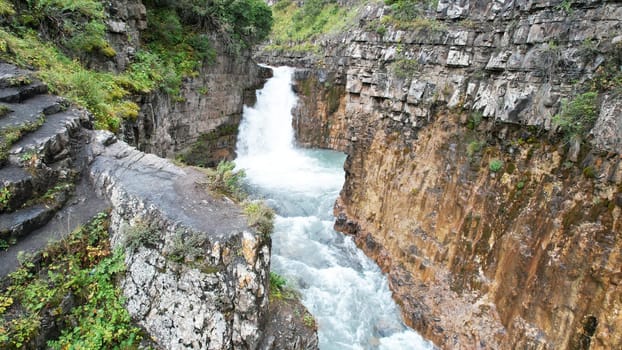 Stunning waterfall cascading down into a narrow canyon, featuring intricately carved stone steps along the side, creating a breathtaking display of nature's beauty and power
