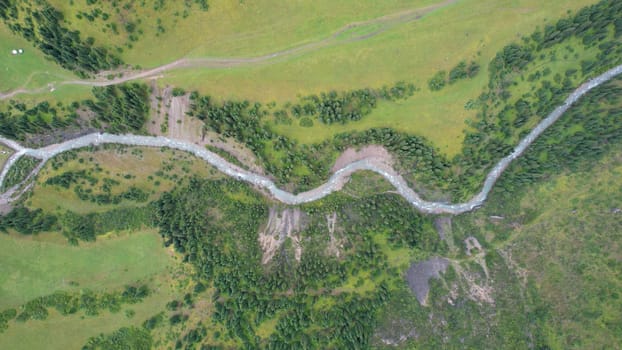 Aerial view capturing a river meandering through a lush green valley, embraced by majestic mountains and dense forests, creating a serene and picturesque natural landscape