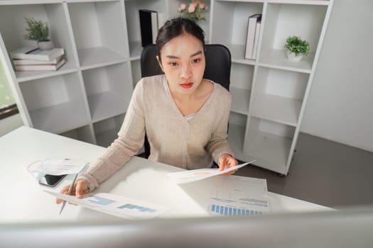 A professional office worker examines financial documents and charts, highlighting focus and analytical skills in a modern office environment.