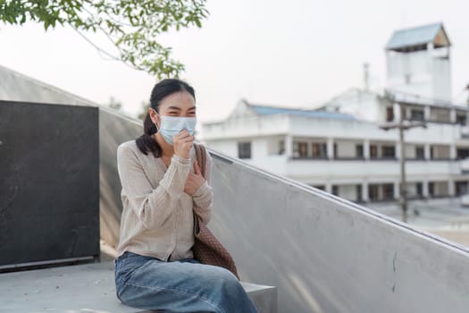 A young woman in a mask sits outside, expressing discomfort from pollution while maintaining a positive demeanor.