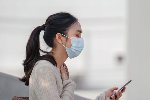 A young woman wearing a face mask checks her phone outdoors, reflecting health awareness in response to pollution.