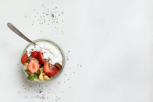 Greek yogurt, nuts and strawberries in a glass jar with a spoon on a white table top view. Healthy breakfast with fruits and nuts. Great way to eat protein