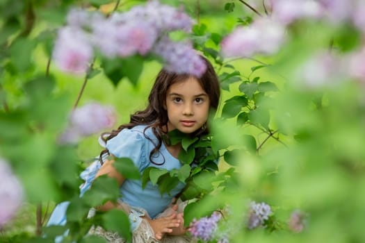 Young hispanic girl in blue dress among lush greenery and pink flowers.