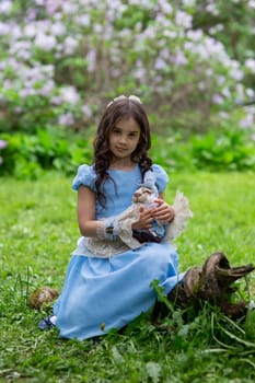 Young caucasian girl in blue dress holding doll in garden setting.