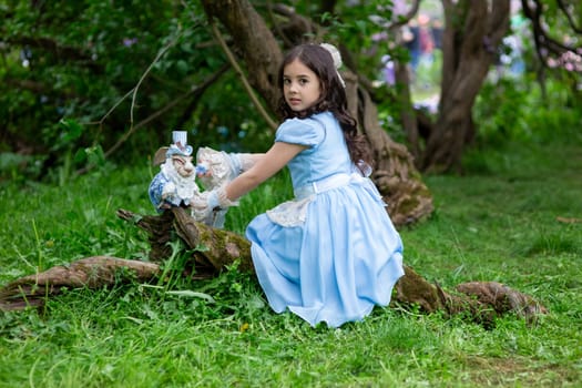 Pretty young girl in blue dress playing in forest with figurine.
