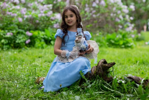 Caucasian young girl in blue dress holding rabbit toy in garden.