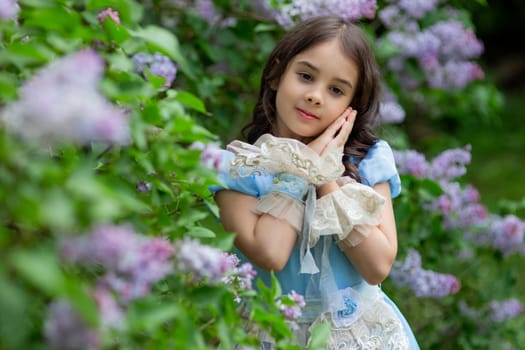 Young caucasian girl in blue dress with lilac flowers in garden.