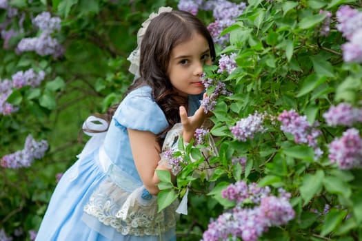 Young caucasian girl in blue dress admiring lilac flower in garden setting.