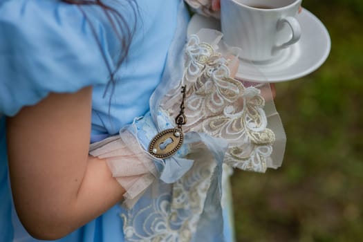 Young girl in blue victorian dress holding teacup in garden setting.