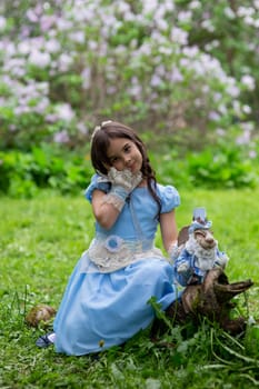 Caucasian female child in blue dress with rabbit doll in garden setting.