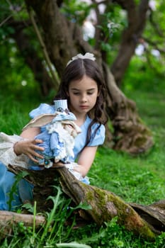 Young caucasian girl in blue dress with plush rabbit in green forest setting.
